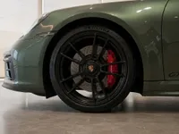The front wheel and fender of a gloss Aventurine Green Metallic Porsche 911 GTS with red brake calipers, visible in Zurich.