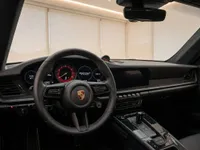 The Porsche 911 Carrera 4 GTS Aerokit's luxurious black interior is visible from the driver's perspective, showcasing the steering wheel, digital dashboard, and sleek center console in Zurich.