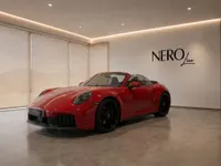 The red Porsche 911 Carrera 4 GTS Cabriolet is parked in a modern showroom in Zurich, top down.