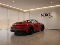 The red Porsche 911 Carrera 4 GTS Cabriolet is parked in a modern showroom in Zurich, viewed from the rear three-quarter angle.