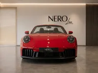 The red Porsche 911 Carrera 4 GTS Cabriolet is seen from the front with its top down in a modern Zurich showroom.