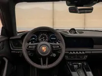 The luxurious interior of the Porsche 911 Carrera 4 GTS Cabriolet in Zurich, highlighting the steering wheel and dashboard with red stitching.