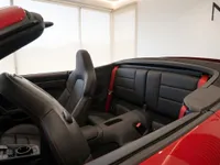 The Porsche 911 Carrera 4 GTS Cabriolet interior in Zurich, showcasing black leather seats with red stitching, red seatbelts, and the retracted top.