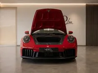 A striking red Porsche 911 Carrera 4 GTS Cabriolet is shown from the front with its frunk open in a showroom in Zurich.