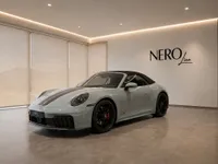 The gloss light grey Porsche 911 Carrera 4 GTS Cabriolet is showcased from the front three-quarter view in a showroom in Zurich.