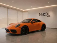 The vibrant orange Porsche 911 Carrera 4S is displayed in a modern showroom in Lausanne, showcasing its sleek design.