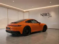 The orange Porsche 911 Carrera 4S is parked in a showroom in Lausanne, showcasing its sleek rear three-quarter view.