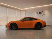 The orange Porsche 911 Carrera 4S is displayed in a modern showroom in Lausanne, showcasing its sleek side profile.
