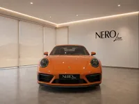 The striking orange Porsche 911 Carrera 4S is presented head-on in a modern showroom in Lausanne.