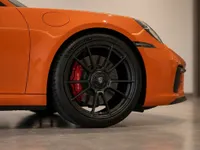 Front wheel of the Gloss Orange Porsche 911 Carrera 4S, featuring a black multi-spoke rim and red brake caliper, in Lausanne.