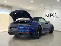 تُرى سيارة بورش 911 كاريرا 4S كابريو الزرقاء موديل 2022 من زاوية خلفية ثلاثية الأرباع مع صندوقها الأمامي مفتوح في إيبيزا.