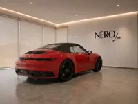 A red Porsche 911 Carrera 4S Cabriolet with its black soft top is displayed in a modern showroom in Lausanne.