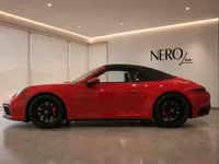 A red Porsche 911 Carrera 4S Cabriolet with its black convertible top up, displayed in a modern showroom in Lausanne.