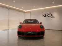 A striking red Porsche 911 Carrera 4S Cabriolet is parked front-on in a modern NEROline showroom in Lausanne.