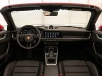 The luxurious interior of the Porsche 911 Carrera 4S Cabriolet in Lausanne, featuring the dashboard, steering wheel, and black leather seats with red stitching.