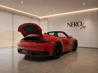 A red Porsche 911 Carrera 4S Cabriolet with its trunk open, parked in a luxury showroom in Lausanne.