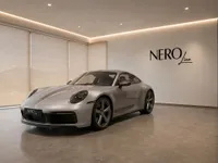 The gloss GT Silver Metallic 2023 Porsche 911 Carrera T is parked in a modern showroom in Zurich, visible from the front three-quarter angle.