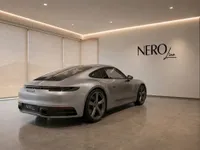 Porsche 911 Carrera T in gloss GT Silver Metallic, viewed from the rear three-quarter angle, parked in a modern showroom in Zurich.