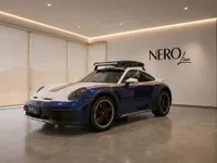 The blue and white Porsche 911 Dakar, equipped with a roof rack and light bar, is showcased in a modern Zurich showroom.