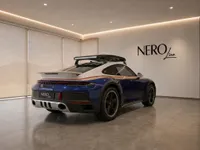 The blue and white Porsche 911 Dakar with gold and red stripes and a roof rack is parked in a showroom in Zurich.