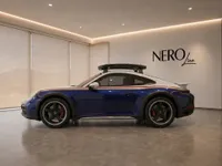 The blue and white Porsche 911 Dakar with gold and red stripes is parked sideways in a modern showroom in Zurich.
