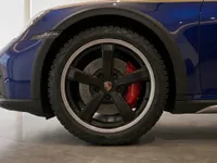 The blue Porsche 911 Dakar's front left wheel with black rim and red brake caliper is prominently displayed in Zurich.