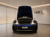 The front view of a blue and white Porsche 911 Dakar with its frunk open, displayed in a modern showroom in Zurich.