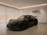 A gloss black Porsche 911 GT3 is parked in a modern showroom with the NeroLine logo and large windows revealing mountains in Lausanne.