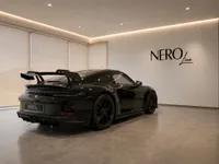A black Porsche 911 GT3, seen from a rear three-quarter angle, displayed in a modern NEROline showroom in Lausanne.