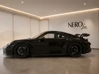 The gloss black 2023 Porsche 911 GT3 is showcased in a modern showroom in Lausanne, viewed from its elegant side profile.