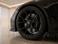 Close-up of the gloss black front wheel and brake caliper of a 2023 Porsche 911 in Lausanne.