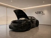 Black Porsche 911 GT3 with its front hood open, revealing the frunk, displayed in a modern showroom in Lausanne.
