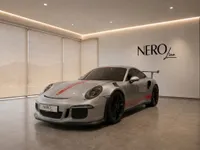 A gloss silver Porsche 911 GT3 RS with red racing stripes, presented from a front three-quarter view in a modern studio in Zurich.