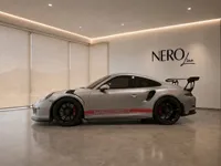 A silver Porsche 911 GT3 RS with red side stripes is parked in a modern showroom in Zurich.