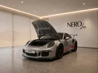 A silver Porsche 911 GT3 RS (991.1) is showcased from a front-three-quarter view with its frunk open in a modern Zurich showroom.
