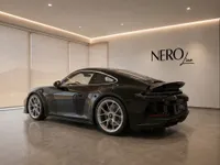 Gloss black Porsche 911 GT3 Touring from the rear three-quarter angle in a modern showroom in Lausanne.