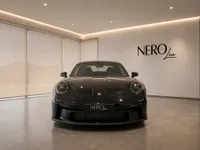 The gloss black Porsche 911 GT3 Touring is showcased from the front view in a modern showroom in Lausanne.