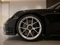 The front quarter view of the black Porsche 911 GT3 Touring in Lausanne, highlighting its silver multi-spoke wheel and brake caliper.