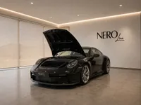 The black Porsche 911 GT3 Touring with its front frunk open is displayed in a modern showroom in Lausanne.