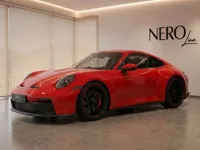 The red Porsche 911 GT3 Touring is showcased from a front three-quarter view in a modern showroom in Zurich.