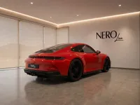 A vibrant red Porsche 911 GT3 Touring is showcased from a rear three-quarter angle in a contemporary Zurich showroom.