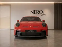 A red Porsche 911 GT3 Touring is prominently displayed from the front in a luxurious showroom in Zurich.