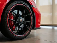 A close-up view of the red Porsche 911 GT3 Touring's front wheel, featuring a black multi-spoke rim with red accents and a prominent red brake caliper, in Zurich.