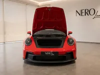 The red Porsche 911 GT3 Touring is shown from the front with its hood open, revealing the front storage compartment in a Zurich showroom.