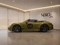 A satin olive green Porsche 911 Spirit 70 convertible is parked sideways in a modern showroom in Zurich.