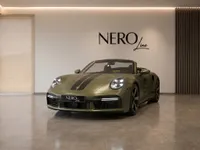 The satin Olive Green Porsche 911 Spirit 70 convertible is displayed frontally in a modern Zurich showroom with the top down.