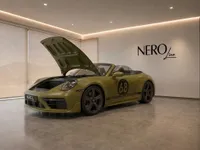 A satin olive green Porsche 911 Spirit 70 convertible with its front hood open, displayed in a modern Zurich showroom.