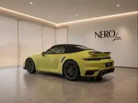 The yellow Porsche 911 Turbo S Cabriolet is showcased from a rear three-quarter angle in a modern Zurich showroom.