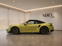 The yellow 2025 Porsche 911 Turbo S Cabriolet is showcased in a side profile view inside a modern showroom in Zurich.