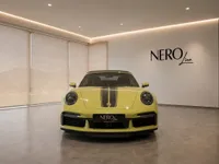 The yellow Porsche 911 Turbo S Cabriolet with black racing stripes is prominently displayed in a modern Zurich showroom.